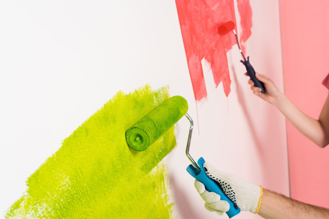 cropped shot of couple painting wall by paint rollers