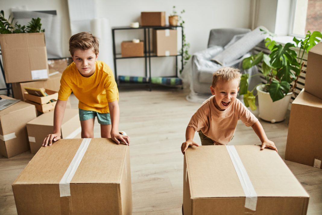 Portrait of two boys sliding cardboard boxes along the floor