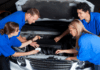 Car Maintenance Tips to Teach Your Teen One adult and four teens stand around a vehicle in blue t-shirts. The adult is teaching car maintenance to teens.