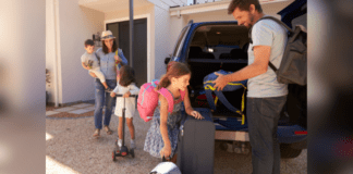 Summer Family Road Trip Essentials A family of two adults and two children are packing items into the back of a car for a road trip.