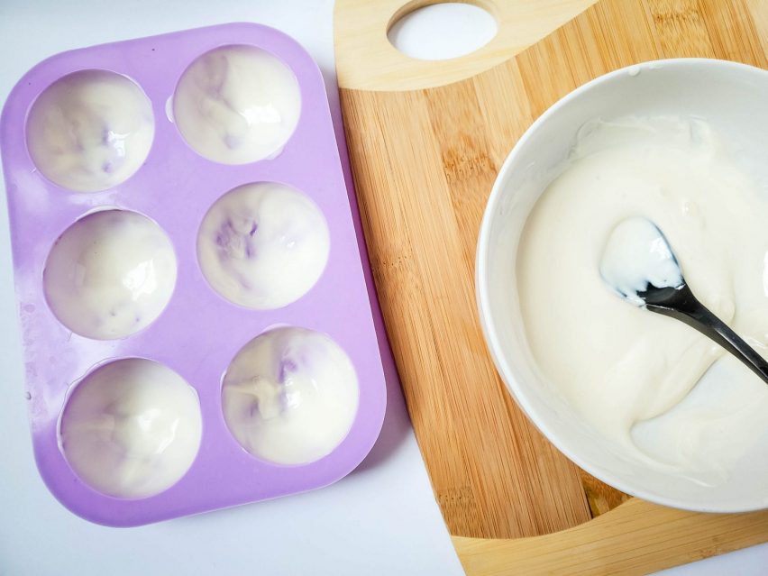 Melted white chocolate in a bowl alondside a silicone mold brushed with white chocolate.