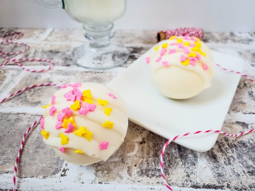 Two white chocolate cocoa bombs with butterfly sprinkles on the top.